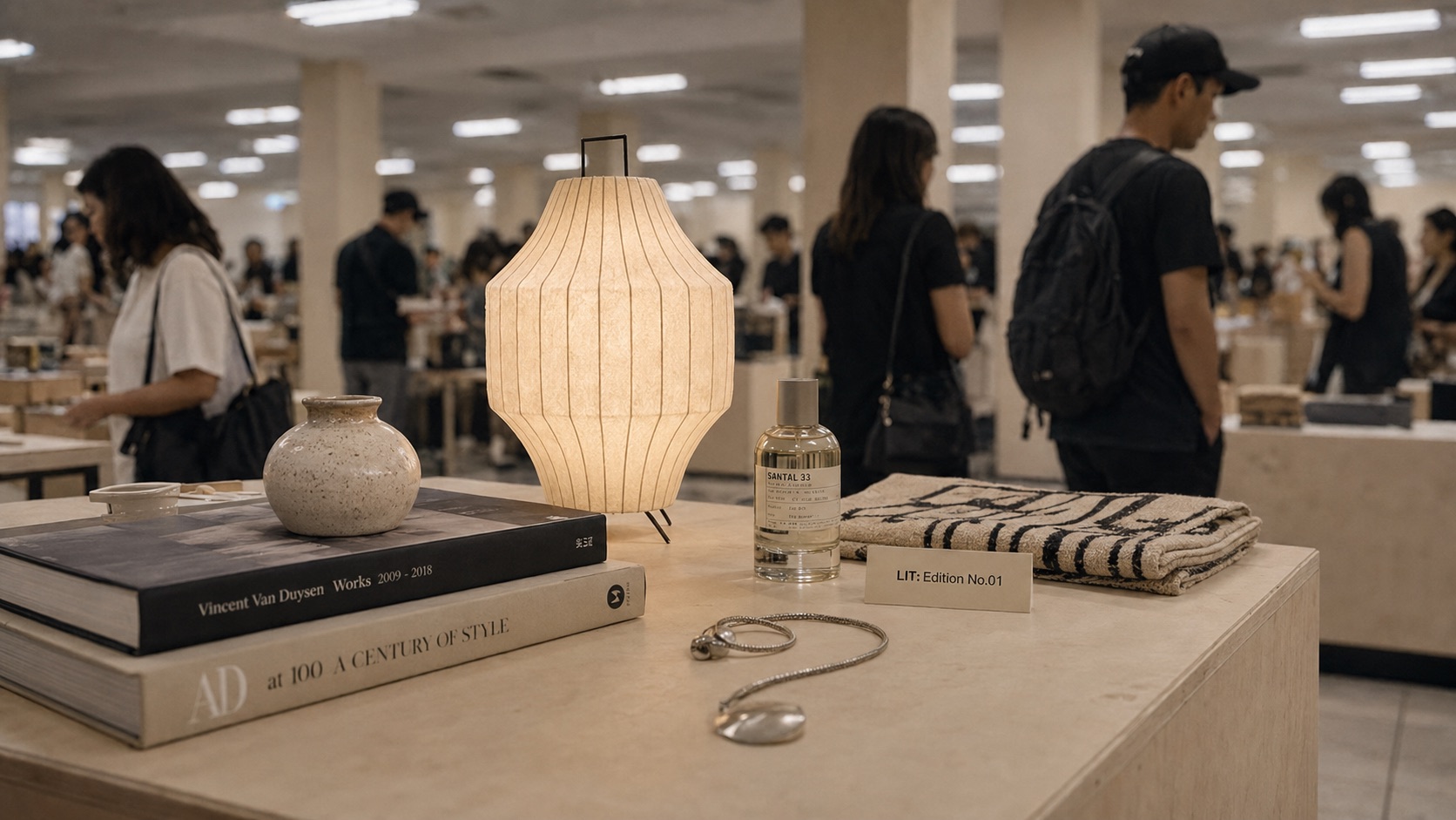 A curated still life of books, a lamp, fragrance, jewellery and textile